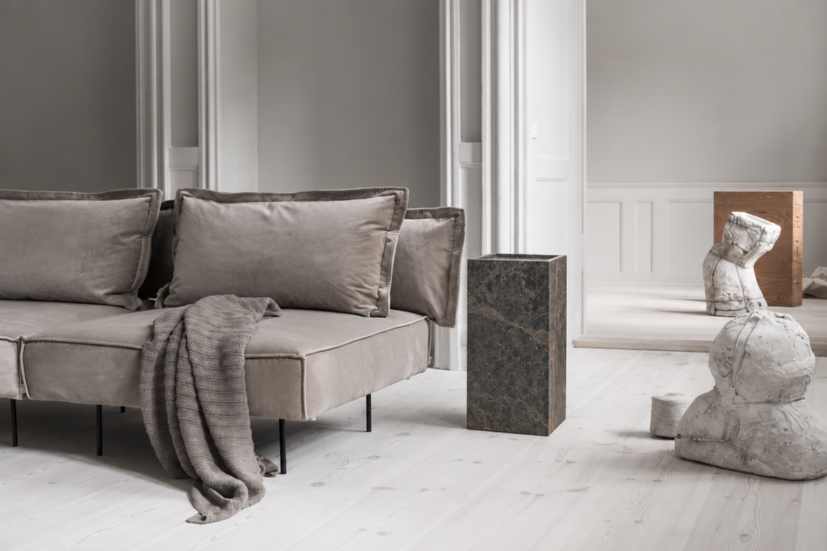 Grey upholstered sofa with soft cushions and a draped throw in a bright, minimalist living room.
